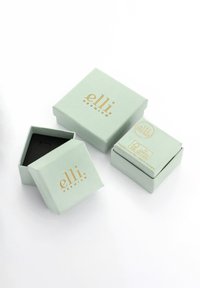 Dve vrhunski škatli v nežno metežno zeleni barvi z zlatim logotipom. Ena škatla je odprta, kar razkriva črno notranjost. Druga škatla je zaprta.