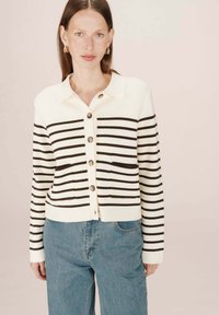 Cardigan rayé en crème et marron foncé, avec un col, une fermeture boutonnée à l'avant et deux poches, fabriqué à partir d'un matériau tricoté doux.