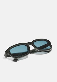 Ochelari de soare cu ramă neagră, cu un design gros și unghiular, și lentile cu nuanță albastră. Material din plastic ușor, cu finisaj lucios.