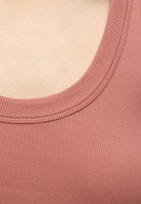 Gros plan sur l’encolure côtelée d’un débardeur rose poudré montrant la texture du tissu et les coutures sur une peau claire.