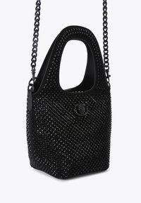 Borsa nera con una superficie texturizzata caratterizzata da piccoli rivetti lucidi. Ha un manico largo, una tracolla a catena e un accento con logo rotondo.