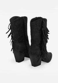 Botas de tobillo de ante sintético negro con detalles de flecos, cremallera lateral y tacón bloque. Las botas cuentan con un diseño elegante y una superficie texturizada.