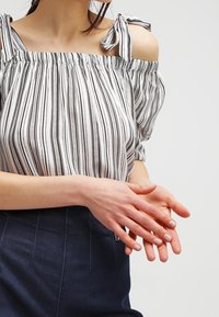 Randig topp med off-shoulder-design, tunna axelremmar och rynkad halsringning. Lätt tyg med vertikala svarta och vita ränder.