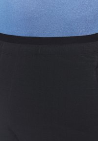 Black pants with a smooth texture, featuring a black elastic waistband. The top portion shows a light blue fitted shirt with a ribbed pattern.