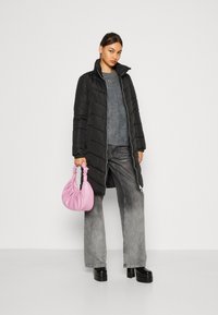 Czarna kurtka puchowa, szary sweter, szare dzwony i masywne czarne botki na platformie; trzyma jasnoróżową torebkę z marszczonym uchwytem.