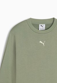 Camiseta de algodón de manga larga en verde oliva con cuello redondo y un pequeño logo bordado blanco en el pecho. Textura suave.
