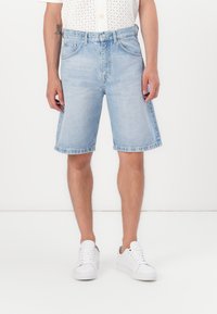 Pantalones cortos de mezclilla azul claro con corte recto, dobladillo deshilachado y diseño de cinco bolsillos, combinados con zapatillas blancas en piernas desnudas.