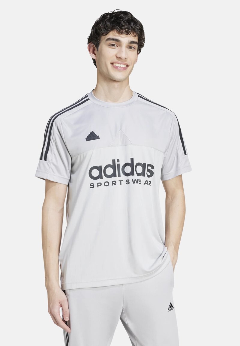 Camiseta deportiva gris de manga corta con logo negro de adidas, diseño de bloques de color horizontal y tres franjas negras en los hombros.