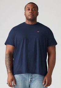 T-shirt en coton marine à manches courtes, col rond, avec un petit logo rouge sur la poitrine gauche. Texture lisse, coupe décontractée.
