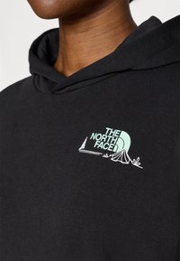 Μαύρο φούτερ με κουκούλα που διαθέτει ένα φωτεινό γαλάζ ιο λογότυπο "The North Face" με γραφικά σκηνής και δέντρου στην αριστερή πλευρά του στήθους.