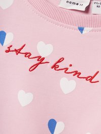 Sudadera rosa con patrones de corazones blancos y azules. "Sé amable" bordado en rojo en el frente. Tejido de algodón suave, cuello redondo.