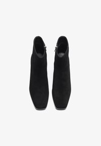 Botas de tobillo de ante negro con punta afilada, que cuentan con un cierre de cremallera y un interior negro suave, diseñadas para un ajuste ceñido.