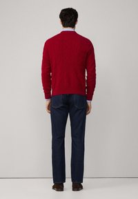 Pull rouge tricoté avec un motif texturé, poignets côtelés et col rond, associé à un jean bleu foncé et des chaussures marron.