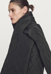 Black quilted puffer jacket featuring a high collar and diagonal stitching. The fabric appears smooth with a lightweight texture.