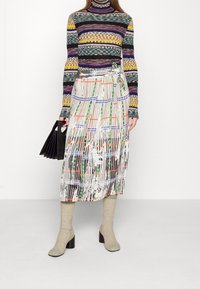 Pull à col roulé à motifs multicolores associé à une jupe midi fluide imprimée avec des rayures verticales et un détail noué ; rehaussé de bottes à talons et d'un sac à main noir.