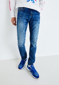 Siniset farkut slim fit -mallissa, joissa on hieman haalistunut pinta ja viisi taskua. Yhdistetty sinisiin urheilukenkiin.