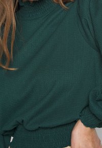 Grön texturerad blus med hög krage, samlade puffärmar och smockad nederkant. Tillverkad av lätt material.