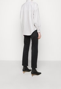 Chemise à rayures avec une coupe décontractée, couleurs crème clair et gris, poignets boutonnés, associée à un pantalon droit noir et des bottines à talons noires.