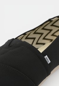Sorte kanvas slip-on sko med teksturert overdel, quiltet design og en kontrasterende zigzag-mønstret innersåle. Merkelapp på siden.