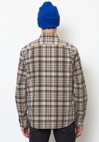 Long-sleeve plaid shirt in beige, brown, and blue tones; features a button-down collar and single-button cuffs. Paired with a blue beanie.