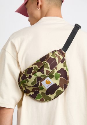 Bolso bandolera de camuflaje en tela verde y marrón, con forma curved, correa ajustable y una etiqueta de logo en el lateral.