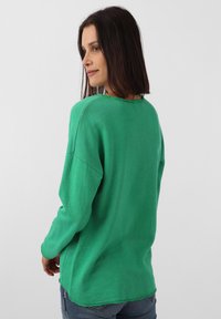 Grüner, langärmeliger Sweatshirt mit ausgefranstem Kragen und Saum, ausgestattet mit einer lockeren Passform und weichem Material, kombiniert mit blauen Jeans.