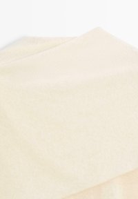 Tissu doux plié de couleur crème claire avec une texture subtile, présenté sur fond blanc.