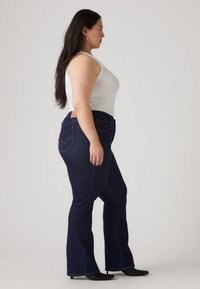 Mørkeblå, høytlivs denim jeans med vide ben, med glatt tekstur, to baklommer og subtile søm detaljer, brukt sammen med en hvit tank topp.