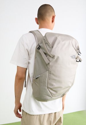 Persoon die een grote lichtgrijze The North Face Kaban LTE rugzak draagt over een wit T-shirt, gezien van achteren tegen een effen achtergrond.