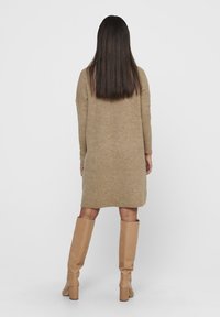 Abito maglione in beige con maniche lunghe, vestibilità comoda e spacchi laterali. Abbinato a stivali beige sopra il ginocchio, creando un look armonioso.