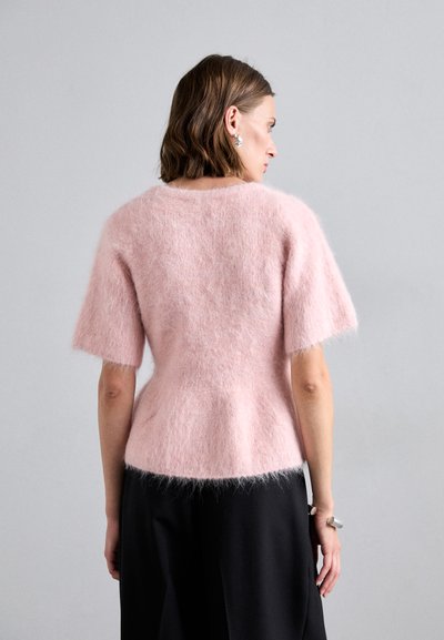 Růžový huňatý svetr s krátkými rukávy, zužující se v pase. Materiál vypadá měkký a strukturální, což kontrastuje s černou sukní.
