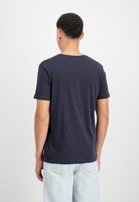 Ναυτικό μπλε βαμβακερό μπλουζάκι με λαιμόκοψη, κοντά μανίκια και λείο ύφασμα, φορεμένο με ανοιχτό μπλε τζιν, από πίσω.