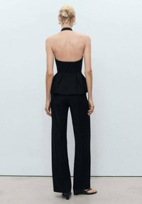 Černý halter top s peplum pasem, v kombinaci s kalhotami s vysokým pasem. Vyznačuje se štíhlým designem a hladkou strukturou. Minimalistický styl.