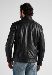 Schwarze Lederjacke mit gesteppten Schulterdetails, schlankem Schnitt, Reißverschlussmanschetten und einer glatten, leicht glänzenden Textur.