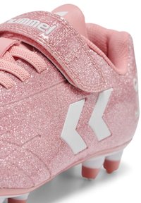 Chaussure de football rose pailletée avec un logo chevron blanc, des lacets roses et une sangle Velcro.