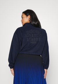 Μπλέ πλεκτό πουλόβερ με ψηλό γιακά. Διαθέτει υφασμένο λογότυπο "adidas ATHLETIC LEAGUE" στην πλάτη. Μακριά μανίκια και χαλαρή εφαρμογή.