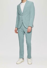 Lichtblauw op maat gemaakt pak met een slanke pasvorm, gestructureerde stof, colbert met één knoop en bijpassende broek, gecombineerd met witte sneakers.