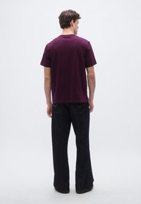 Burgundy short-sleeve t-shirt with a round neckline, paired with loose, dark denim jeans, featuring back pockets and hem stitching.