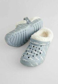 Lichtblauwe klompen met witte vossenpatronen, een pluizige voering, ventilatiegaten en een band. Gestructureerde rubberen zool voor grip.