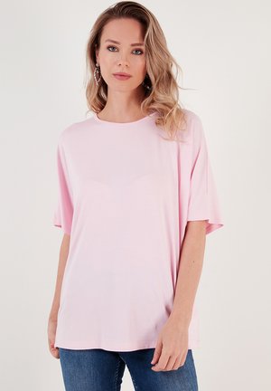 Light pink short-sleeve T-shirt with a round neckline. The fabric appears soft and smooth, worn with blue jeans. Simple and relaxed design.