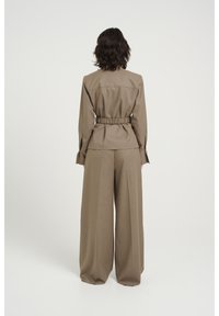 Veste marron sur mesure avec taille cintrée et pantalon large assorti. Tissu lisse avec un design structuré et une coupe décontractée.