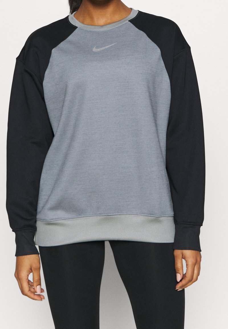 Personne portant un sweat-shirt Nike bicolore avec devant et poignets gris et manches noires, associé à un legging noir, debout les mains détendues.