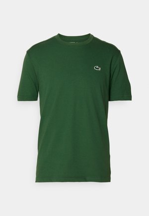 Camiseta de algodón verde con mangas cortas, cuello redondo y un pequeño logo de Lacoste en el lado izquierdo del pecho. Textura suave, diseño casual.