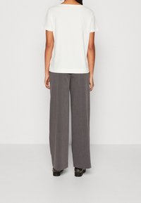 Camiseta blanca de manga corta combinada con pantalones grises de pierna ancha, confeccionados con una tela ligera y texturizada, con detalles del dobladillo visibles en el borde de la camiseta.
