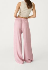 Pantalon large rose clair en tissu texturé, doté d'une taille élastique pour le confort et d'un design fluide.