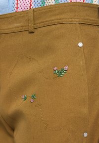 Brune stofferbukser med blomsterbroderi i grønne stilker og pink blomster, pyntet med en sølv knapp på siden.