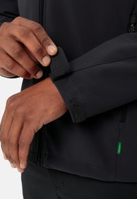 Dark fabric jacket with a close-fitting cuff, featuring a Velcro strap. Includes a zipper and a small green label on the side.