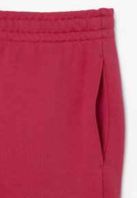 Pantalones de chándal rojos en una suave mezcla de algodón, con cinturilla elástica, bolsillo lateral y textura lisa. Sin patrones ni acentos visibles.