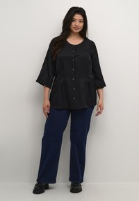 Blusa negra de botones con mangas tres cuartos, que presenta una tela texturizada y un corte holgado, combinada con unos pantalones vaqueros oscuros de corte amplio.