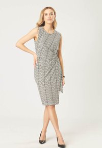 Zwart-witte bloemenpatroon mouwloze jurk met een aansluitende silhouet en een knoopdetail op de taille; gecombineerd met zwarte hoge hakken.